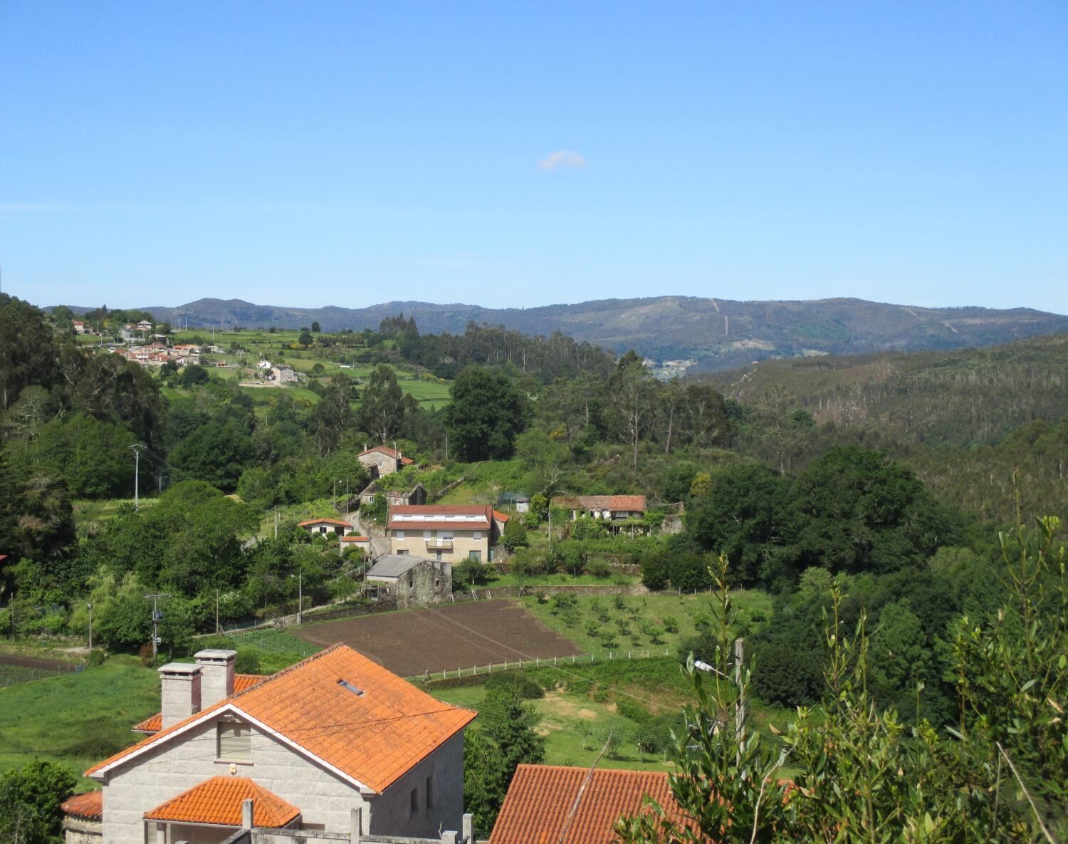 A rural landscape with houses, green fields, and hills in the background.