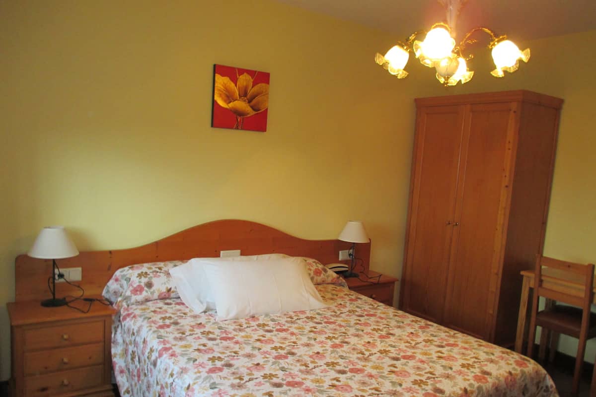 Un dormitorio con colcha estampada, un armario de madera, dos lámparas de noche y un cuadro en la pared.