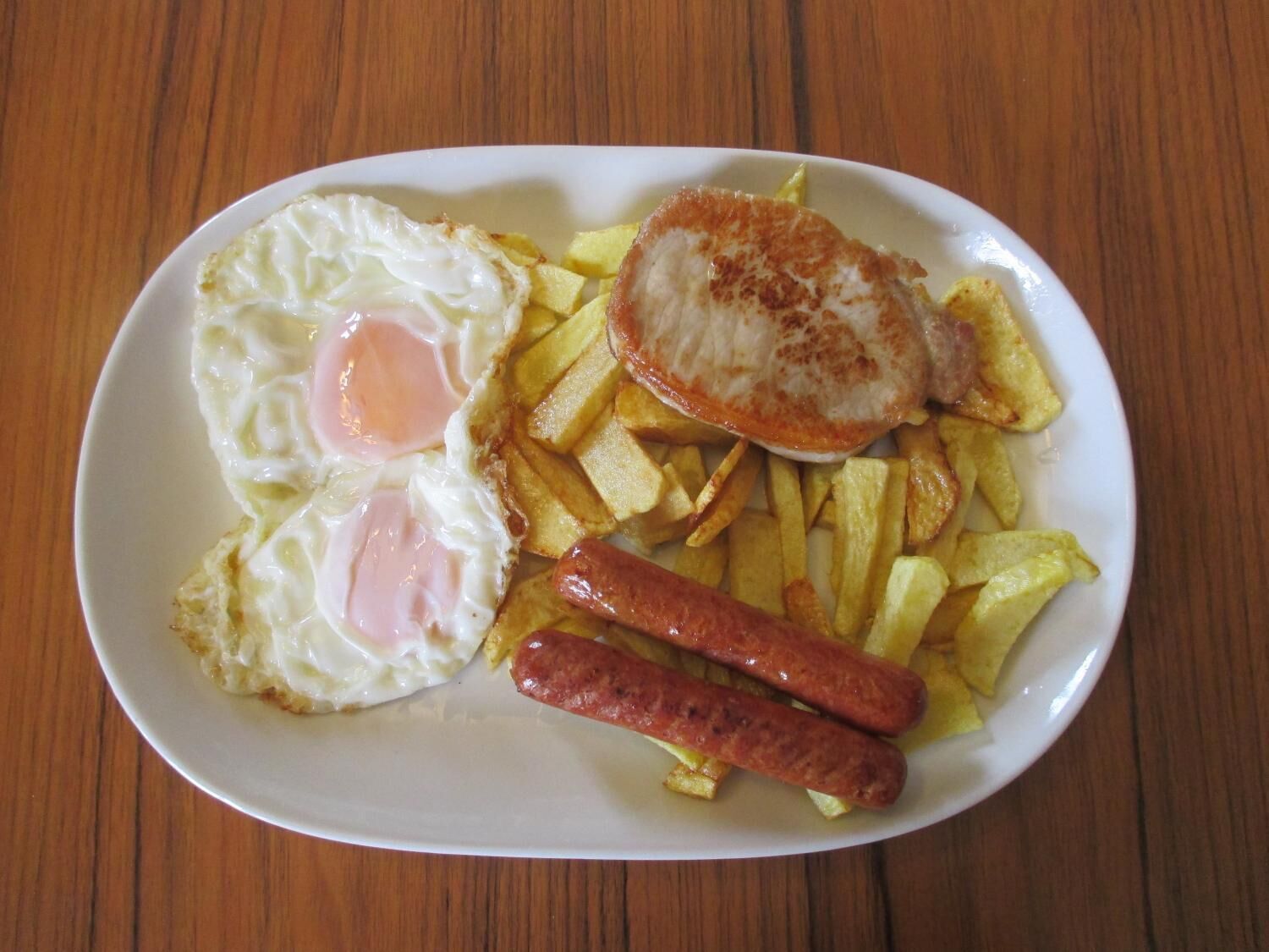 Lautasella on paistettuja kananmunia, perunaraastetta ja makkaroita.