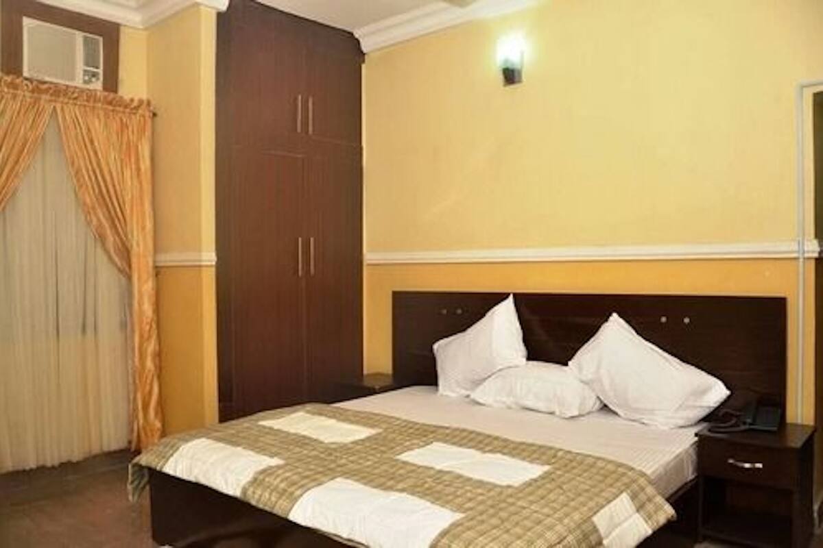 A hotel room with a bed, a nightstand, a wardrobe, and a wall-mounted light.