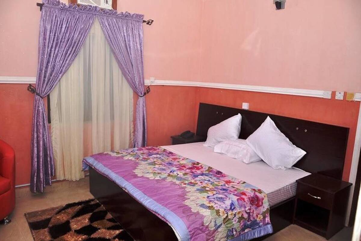 A bedroom with a bed, a nightstand, a red chair, and a decorative curtain.