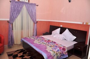 A bedroom with a bed, a nightstand, a red chair, and a decorative curtain. - Birch Tree Hotel (Uyo)