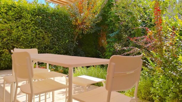 A patio with a white table and chairs, surrounded by lush greenery and a pergola. - Aurora Premium Home (Gyor)