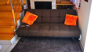 A brown sofa with two orange pillows, a dark carpet, and a wooden staircase. - Aurora Premium Home (Gyor)
