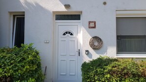 A white door with a small window above it, a wall-mounted light, and a wreath on the right side. - Aurora Premium Home (Gyor)