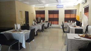 A dining area with multiple tables set for service, air conditioning units, and windows with blinds. - Caesar's Court Hotel and Suites (Abeokuta)