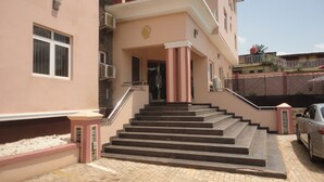 A building with a pink facade, a staircase leading to the entrance, and a car parked nearby. - Caesar's Court Hotel and Suites (Abeokuta)