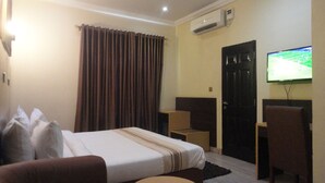 A hotel room with a bed, a TV mounted on the wall, a door, and a window with curtains. - Caesar's Court Hotel and Suites (Abeokuta)