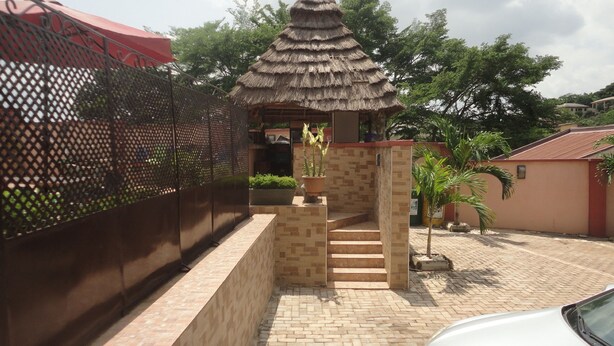 A gated entrance with a thatched-roof structure, a paved pathway, and a small potted plant. - Caesar's Court Hotel and Suites (Abeokuta)