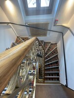 Una escalera de caracol con barandilla de madera y balaustradas de metal, que conduce a un rellano con tragaluz arriba.