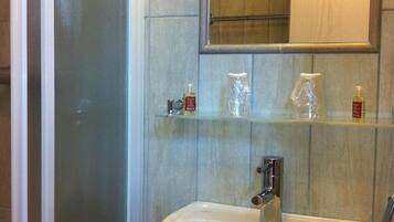 A bathroom with a glass shower enclosure, a sink, and a mirror above a shelf with toiletries.