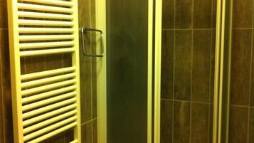 Ducha con cerramiento de vidrio, toallero blanco y puerta de vidrio.