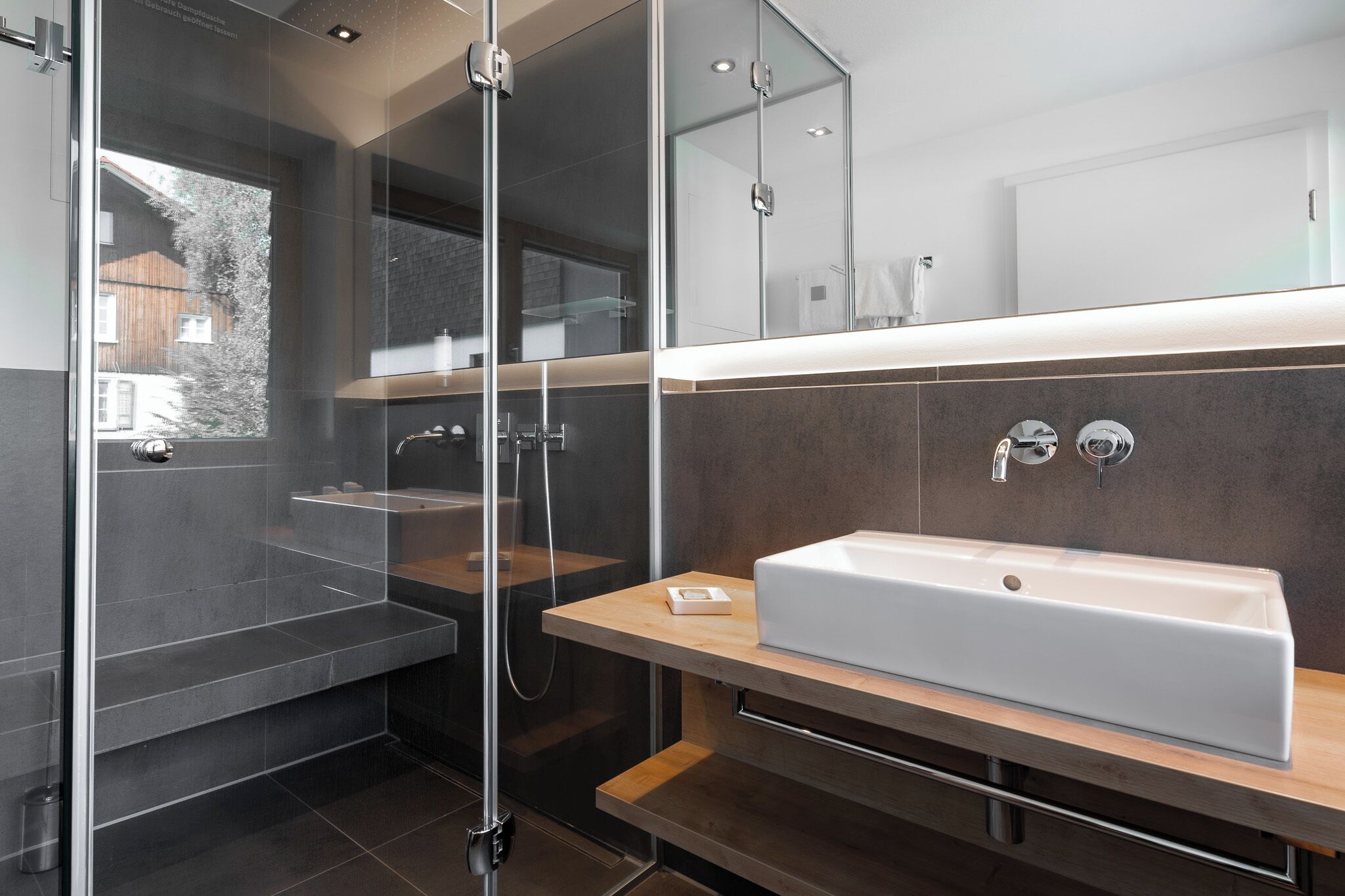 A modern bathroom with a glass-enclosed shower, a large white sink, and a wooden vanity.
