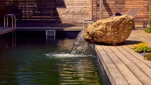 Una terraza de madera con una roca y una piscina.
