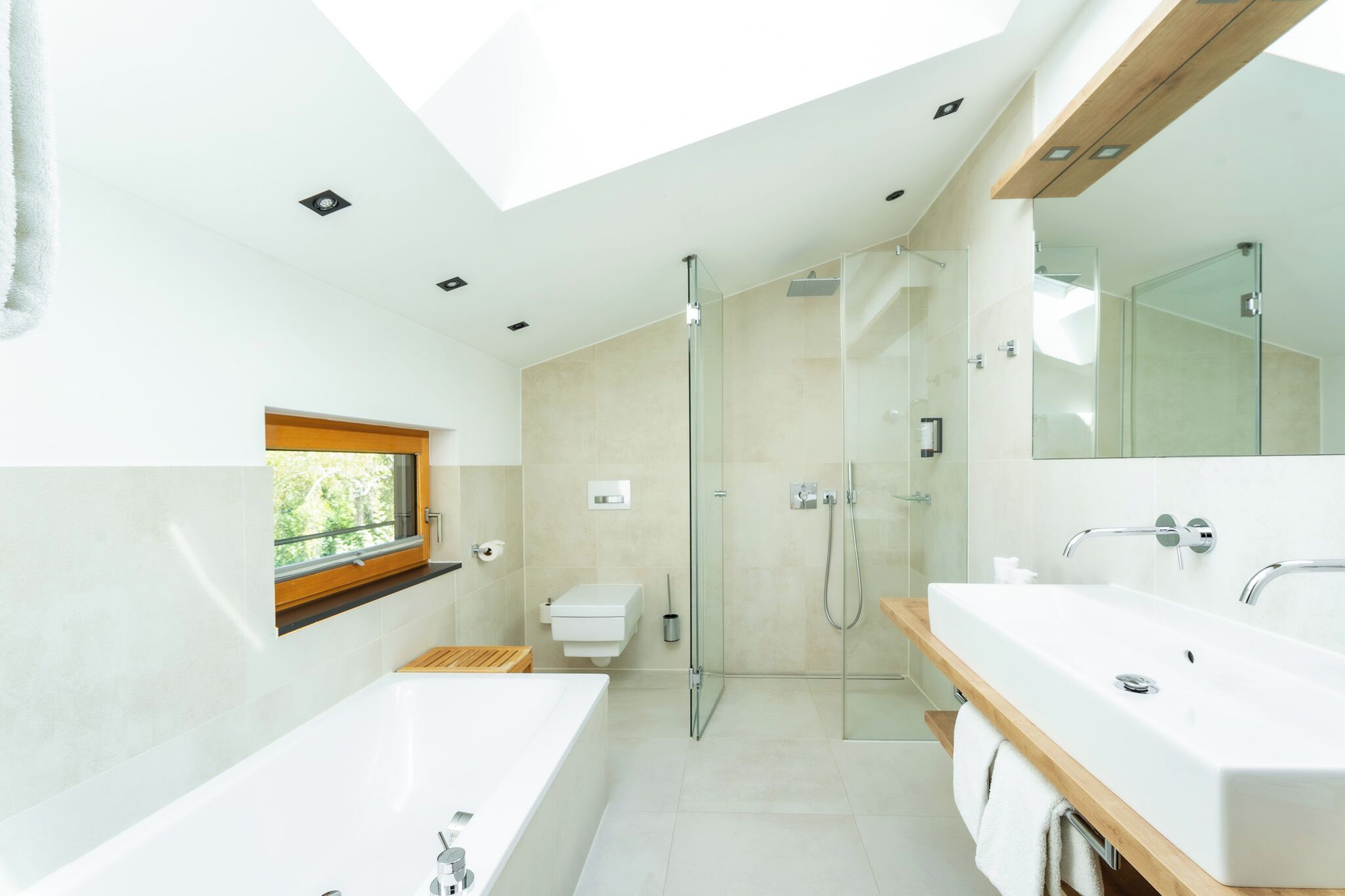 A modern bathroom with a skylight, a large bathtub, a glass-enclosed shower, and a wooden vanity.