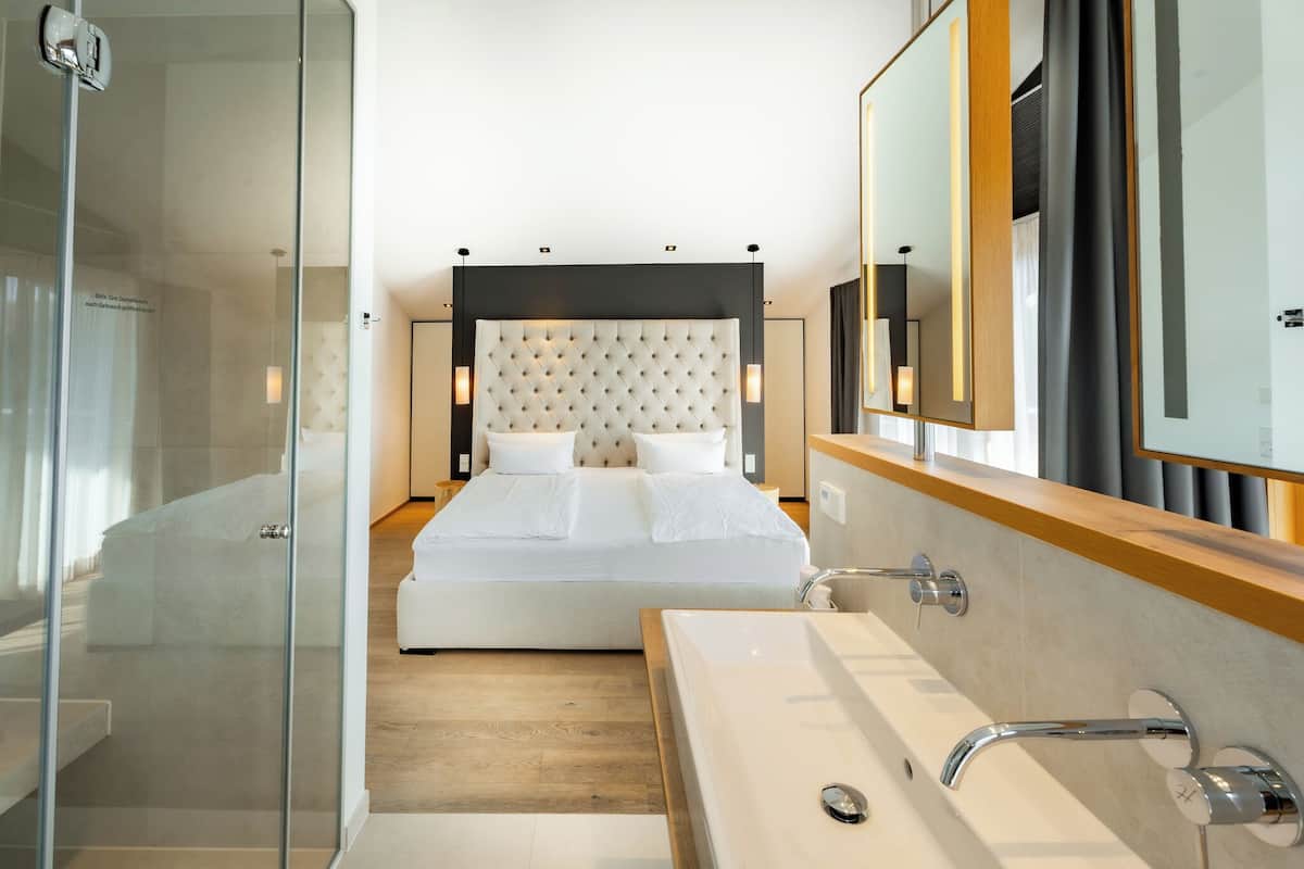 A modern hotel room with a large bed, a glass shower enclosure, and a large mirror.