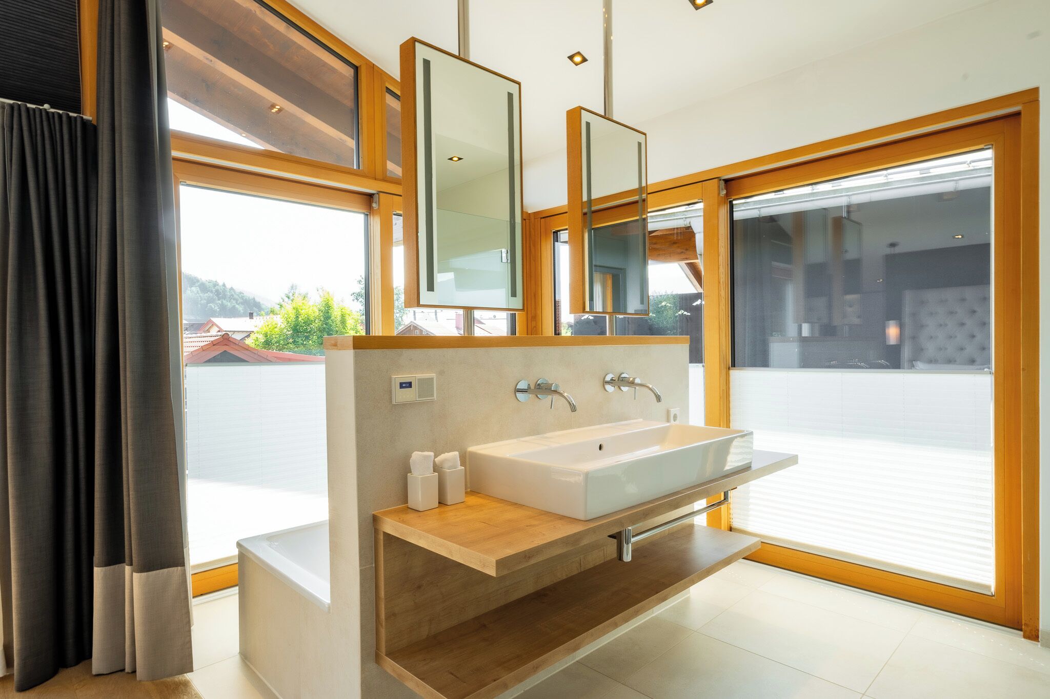 Une salle de bain moderne avec une grande fenêtre, un meuble-lavabo en bois, un lavabo blanc et un miroir.