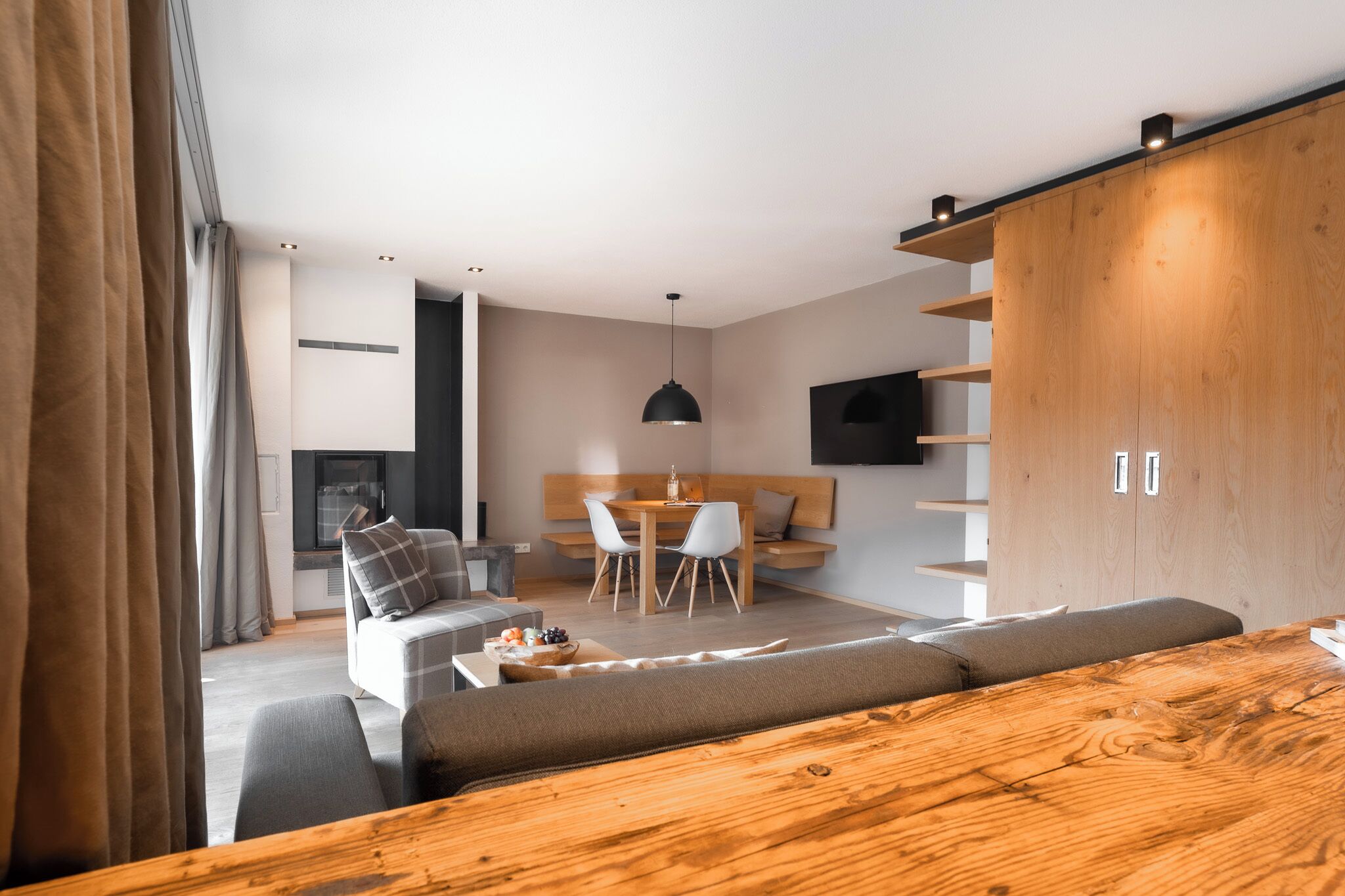 Una sala de estar moderna con una mesa de comedor de madera, un sofá y un televisor montado en la pared.