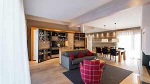 Una sala de estar moderna con un sofá gris, cojines rojos, un sillón rojo a cuadros y una zona de comedor con una mesa y sillas de madera.