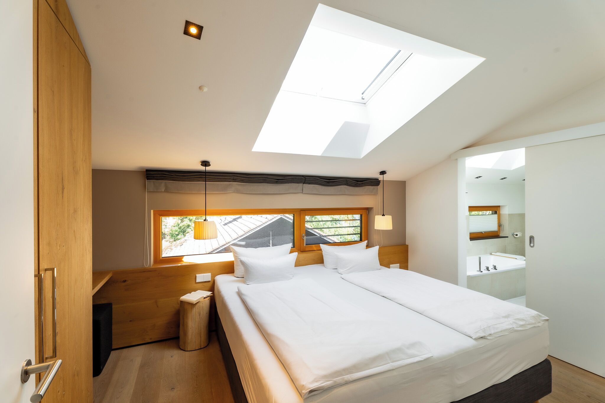 A bedroom with a skylight, a bed, a wooden bench, and a bathroom visible through an open door.