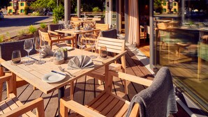 Un espacio para comer al aire libre con mesas y sillas de madera, copas y platos listos para el servicio.