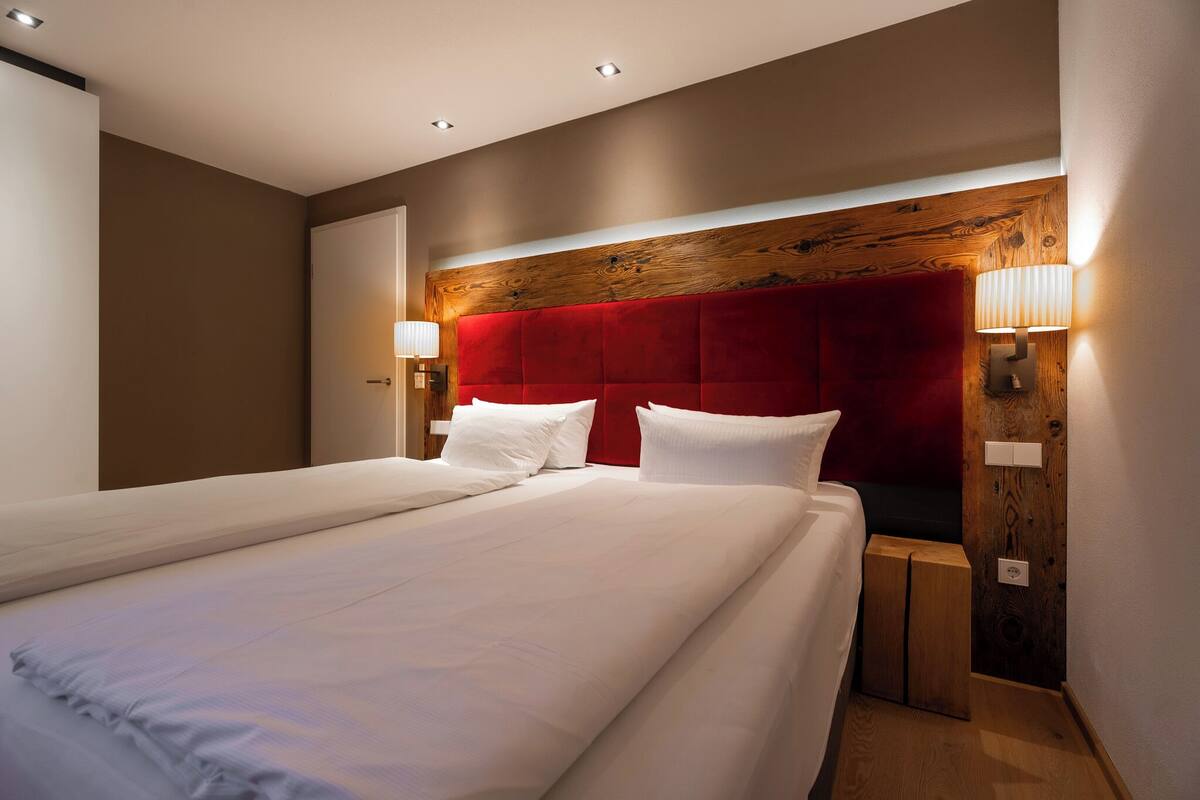 A hotel room with a large bed, wooden headboard, two bedside lamps, and a wooden nightstand.