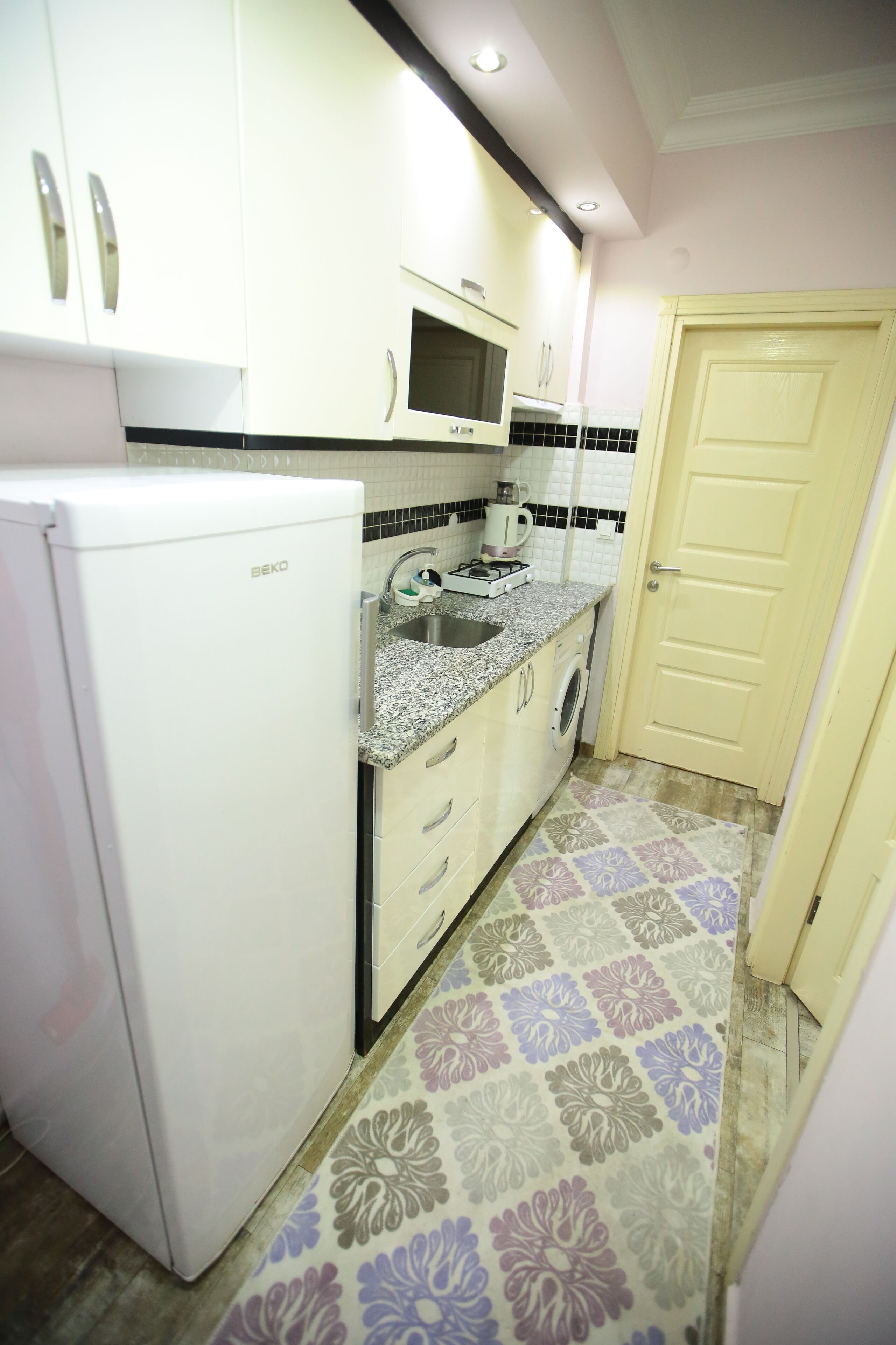 A compact kitchen with white cabinets, a built-in microwave, a sink, and a washing machine.