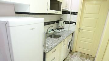 A compact kitchen with white cabinets, a built-in microwave, a sink, and a washing machine.