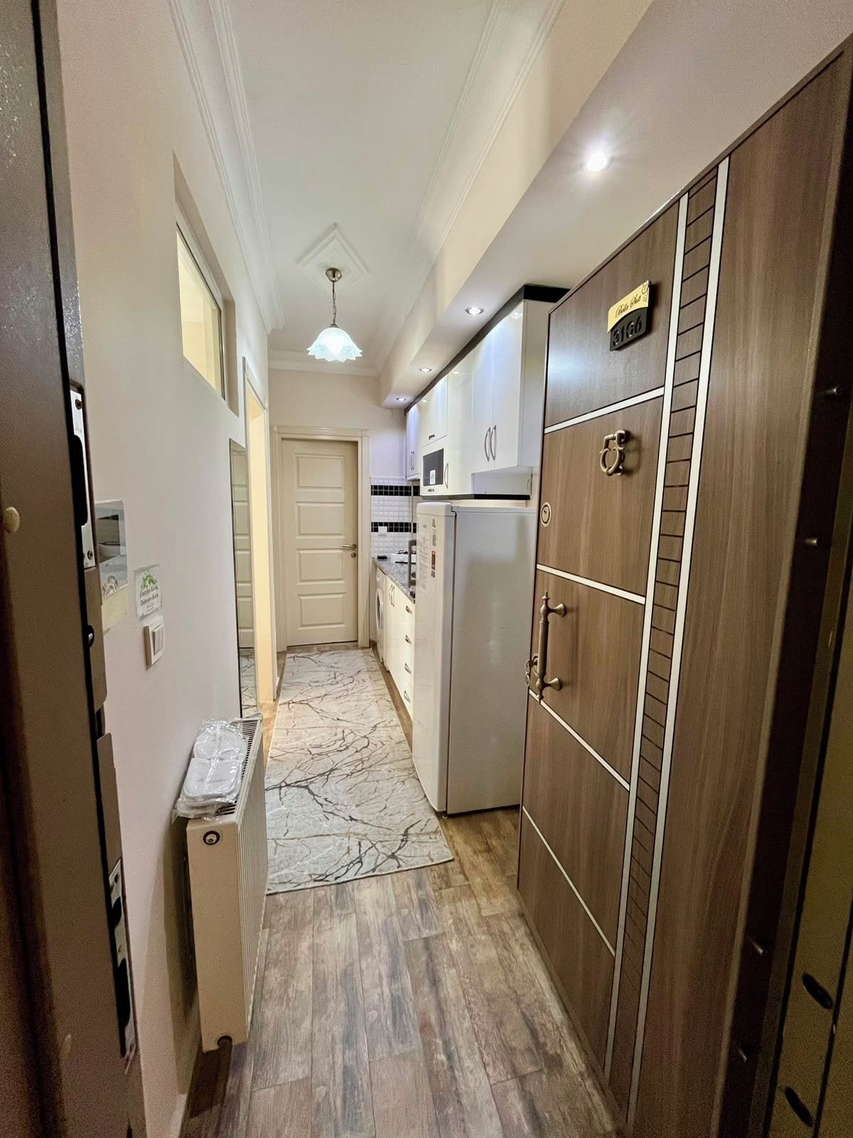 A narrow hallway with a refrigerator, a microwave, and a wooden cabinet.