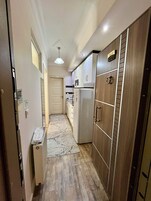 Un pasillo estrecho con un refrigerador, un microondas y un armario de madera.