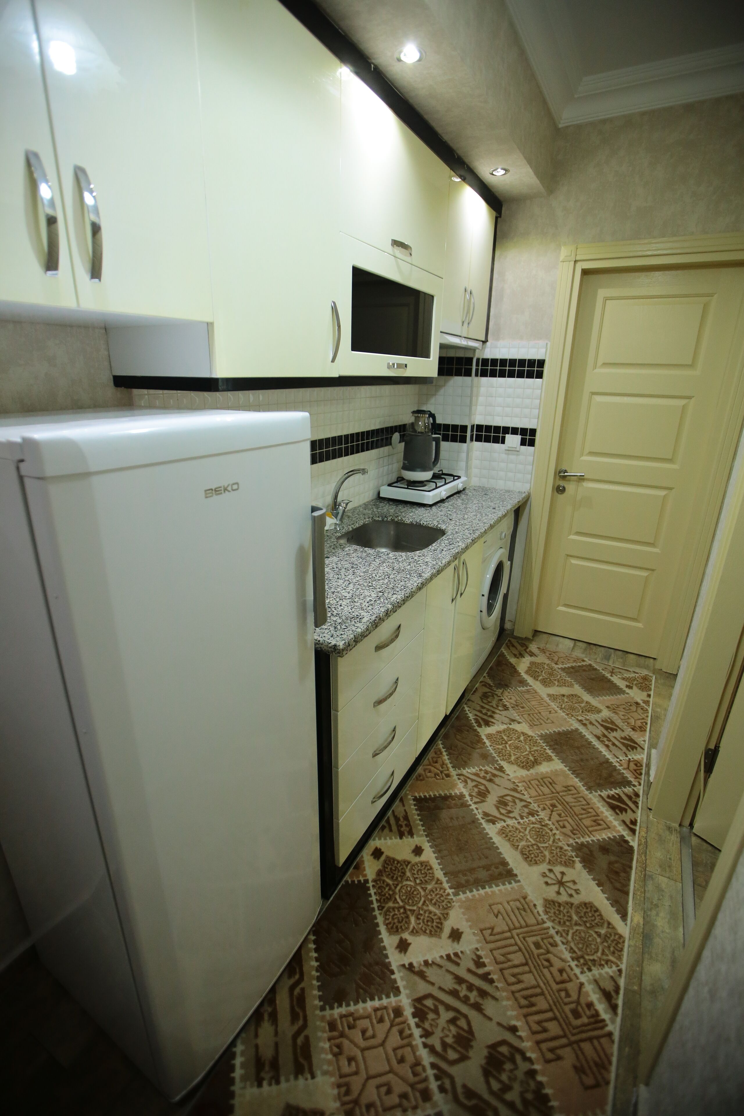 A compact kitchen with a refrigerator, microwave, sink, and washing machine.