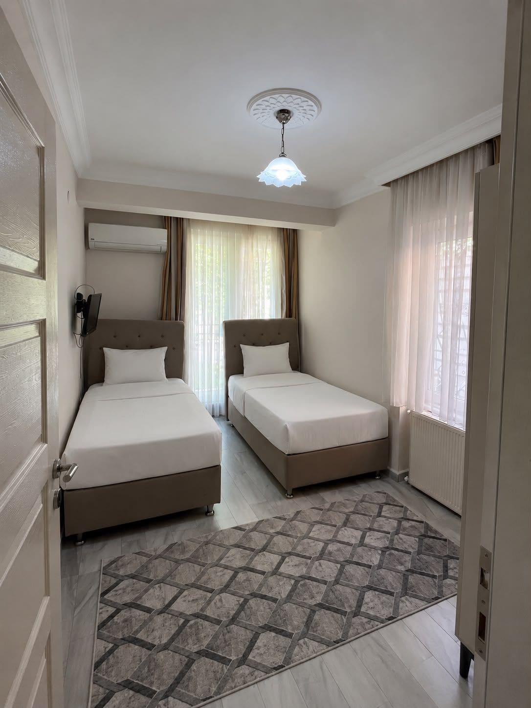 Habitación de hotel con dos camas, una lámpara en el techo, un aire acondicionado de pared y una alfombra estampada.
