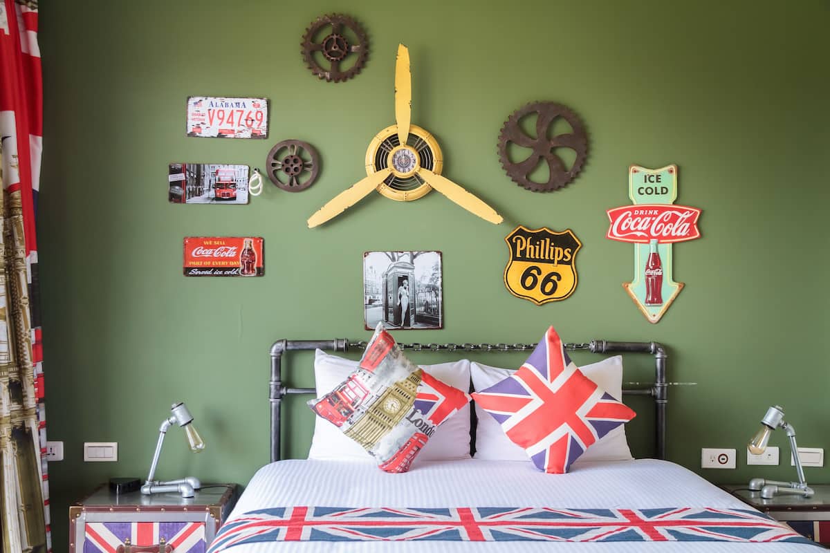 A bed with a Union Jack blanket, pillows with British flags, and wall decor including a clock, vintage signs, and a 'Phillips 68' sign.