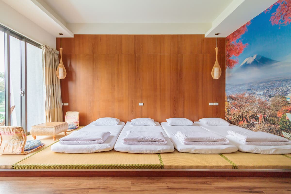 A room with three single beds, a tatami mat floor, a wooden wall, and a large window.