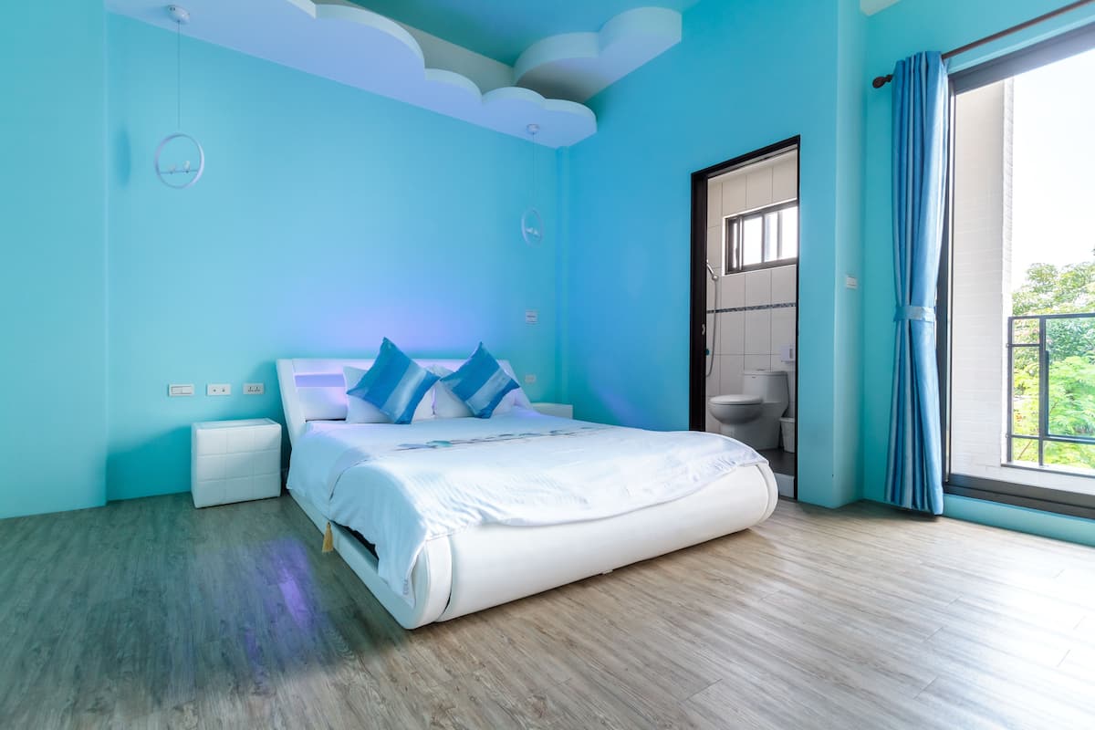 A modern bedroom with a large bed, a nightstand, a wall clock, and a bathroom door.