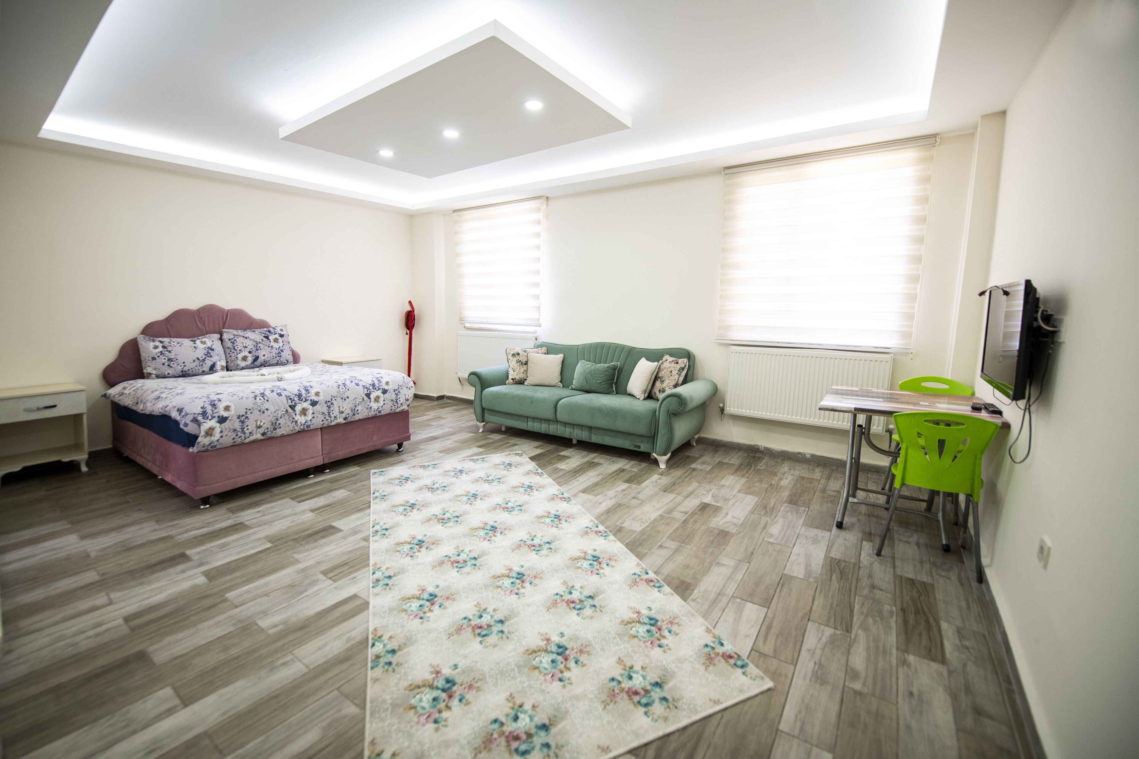 A bedroom with a bed, a green sofa, a small table, and a TV.