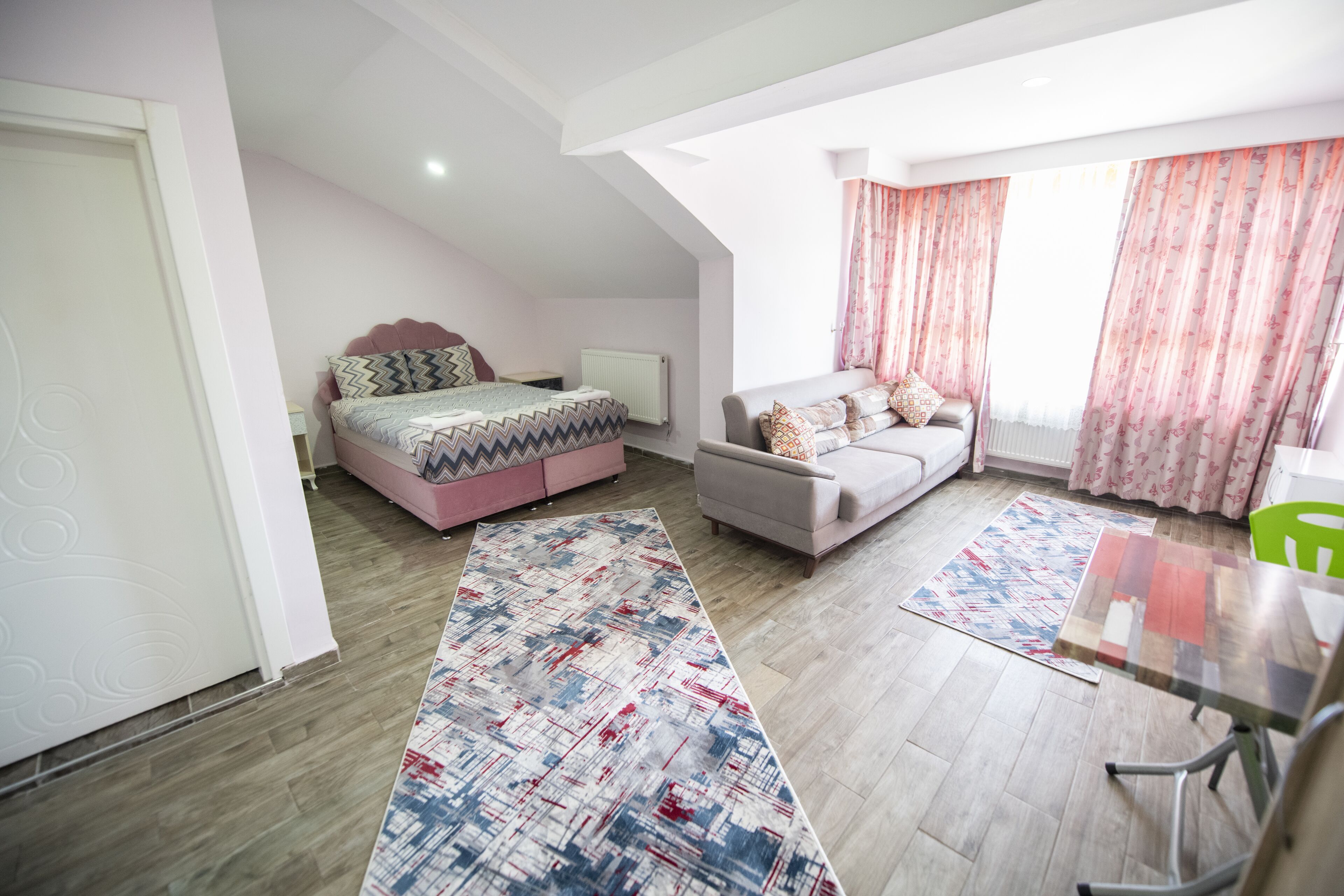 A modern bedroom with a bed, a sofa, a dining table, and a large window with curtains.