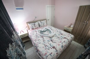 Un dormitorio con edredón floral, una mesita de noche con lámpara, un armario y una puerta con pomo decorativo.