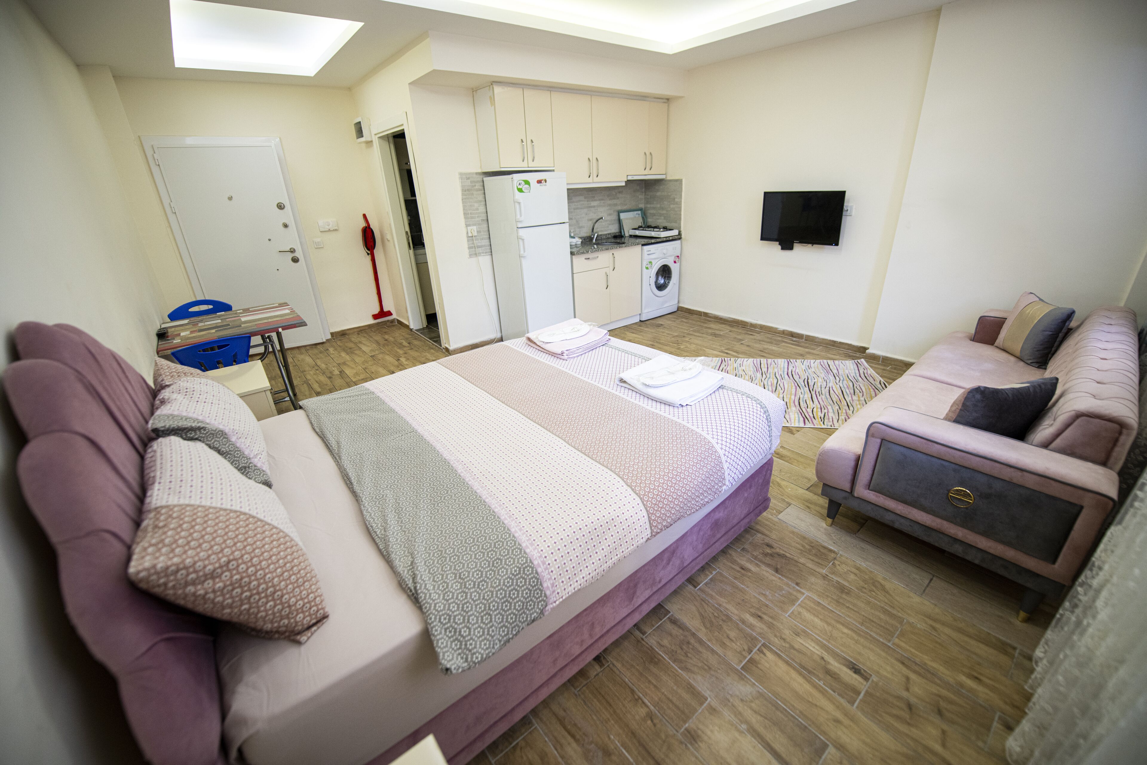 Une chambre moderne avec un grand lit, un canapé, un petit coin cuisine et un lave-linge.