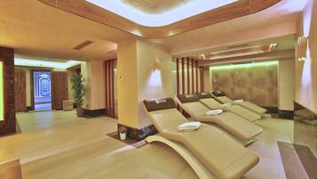A spa room with four reclining chairs, a potted plant, and a reception area visible in the background.