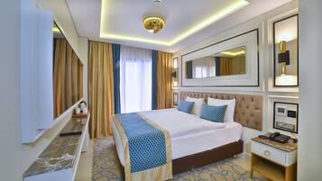 A hotel room with a large bed, a bedside table with a phone and a lamp, a mirror, and a window with curtains.