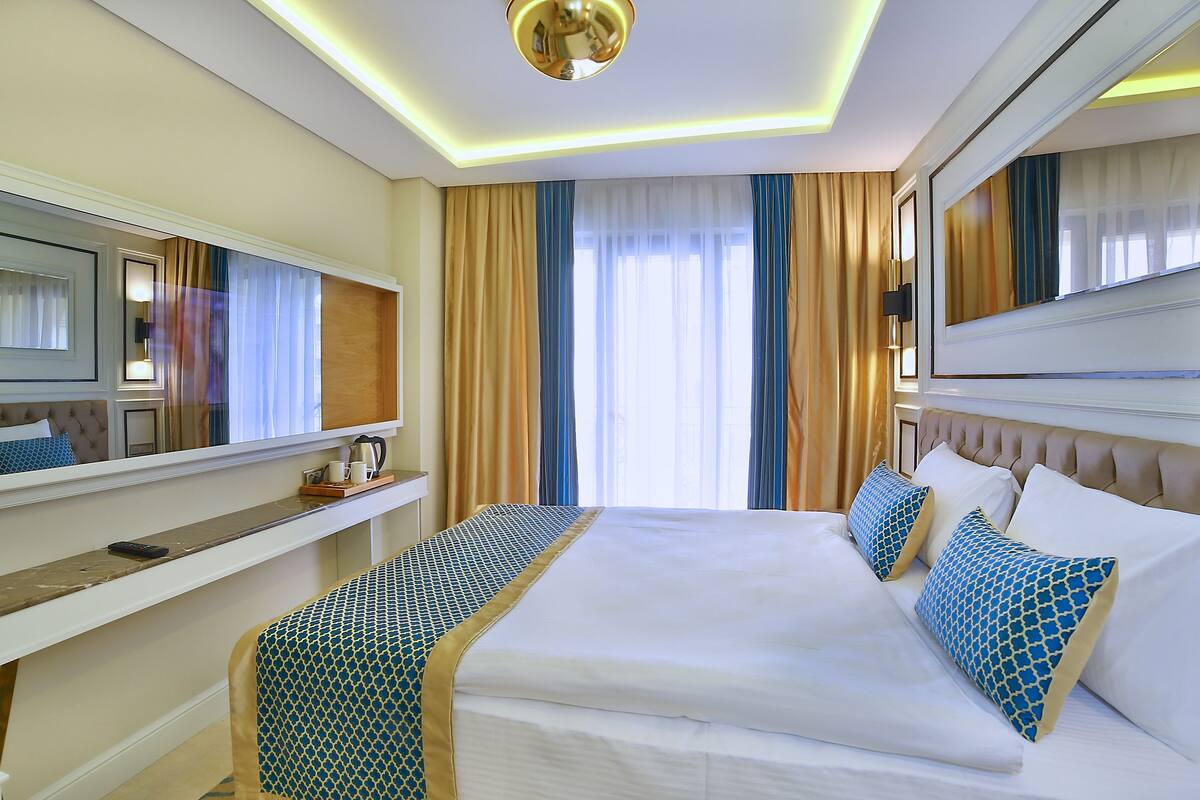 Habitación de hotel con una cama grande, una mesita de noche, un espejo y una ventana con cortinas.