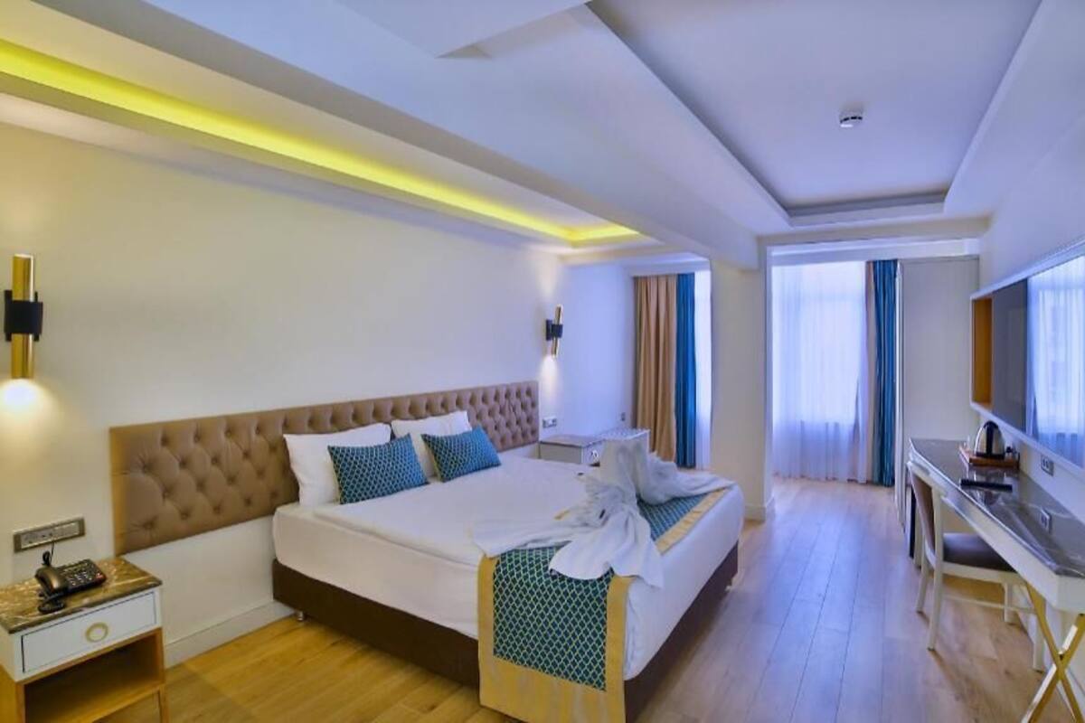 Una habitación de hotel con una cama grande, mesita de noche, escritorio y televisor.