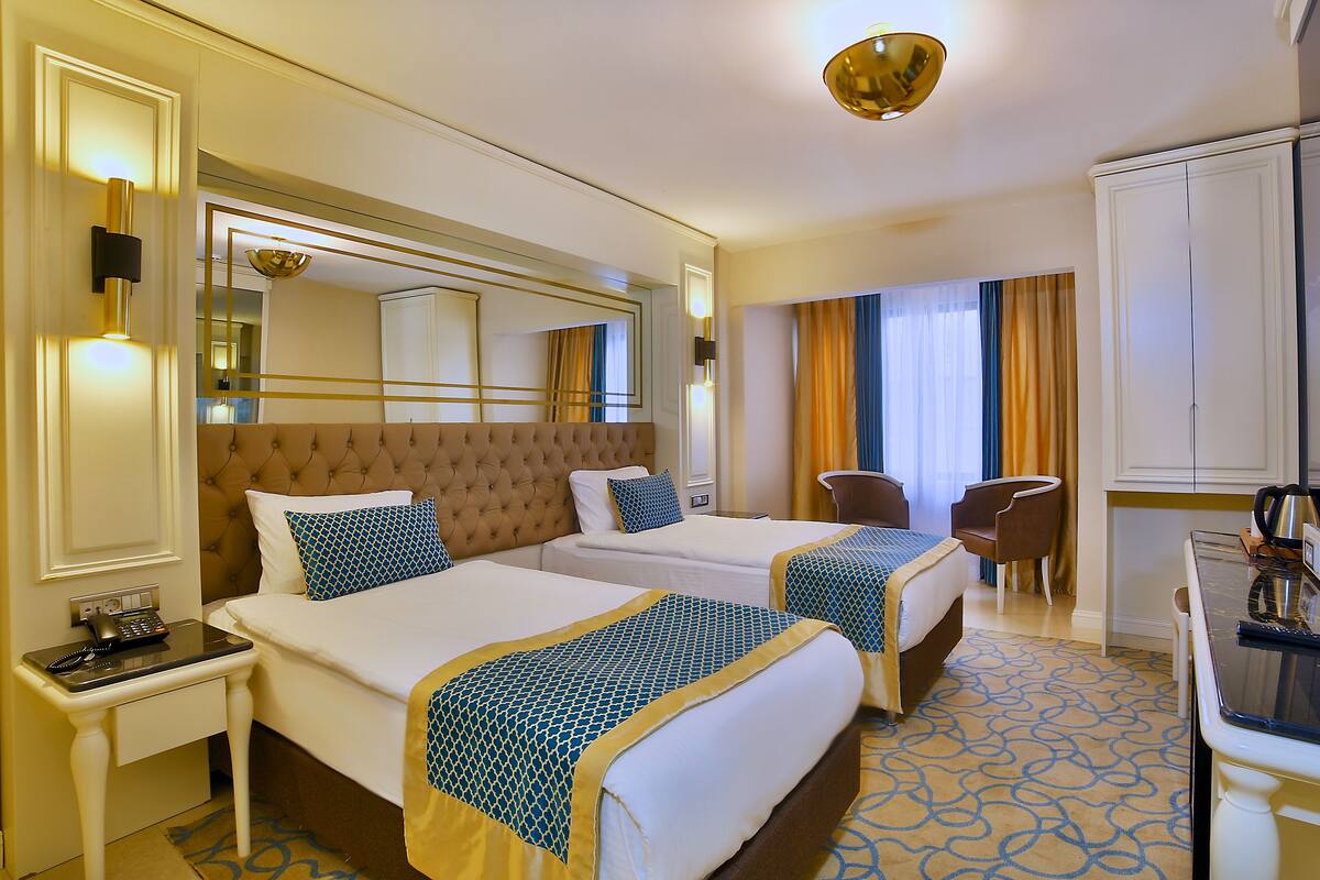 Habitación de hotel con dos camas, un escritorio, una silla, un minibar y un espejo grande.