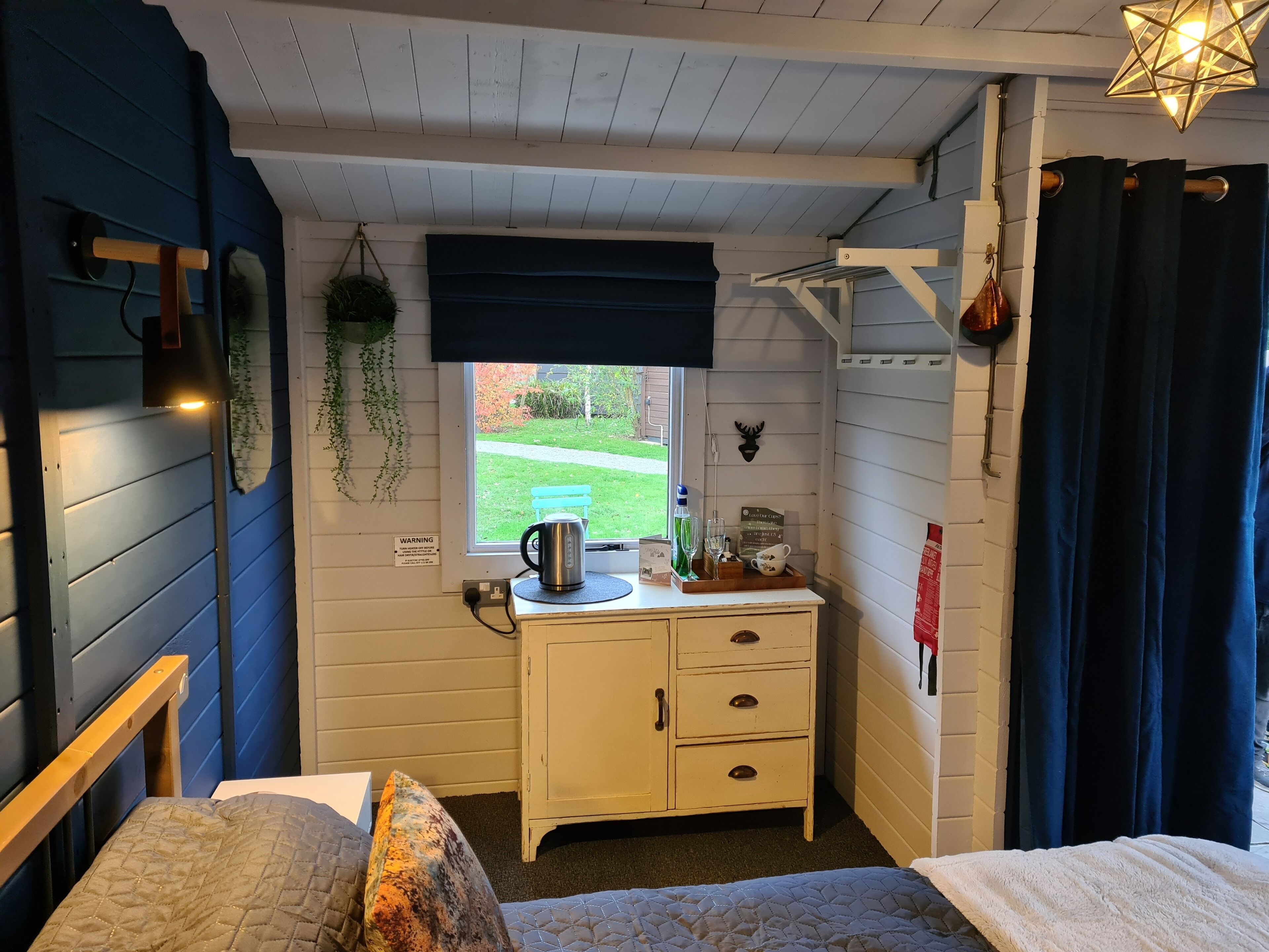 Une petite chambre agréable, dotée d’un lit, d’un bureau avec une bouilloire et d’une fenêtre donnant sur un jardin.