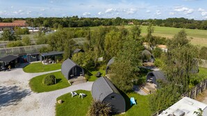 A view of a campsite with several dome-shaped tents, a grassy area with seating, and a backdrop of trees and a clear sky. - The Little Hide - Adult Only Camping Pods (York)