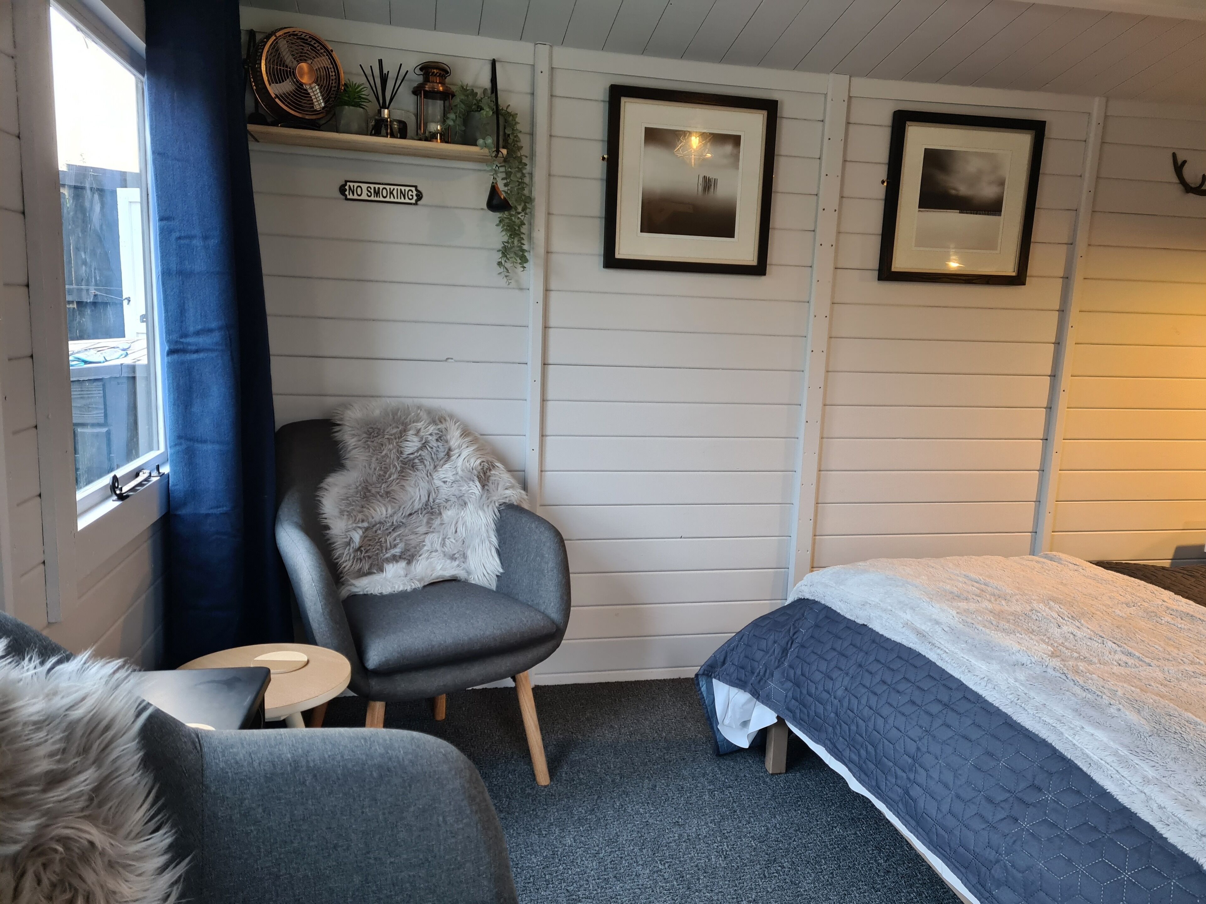 Ein gemütliches Zimmer mit einem Bett, einem Sessel mit weicher Decke, einem kleinen Tisch und einem Rauchverbotsschild an der Wand.