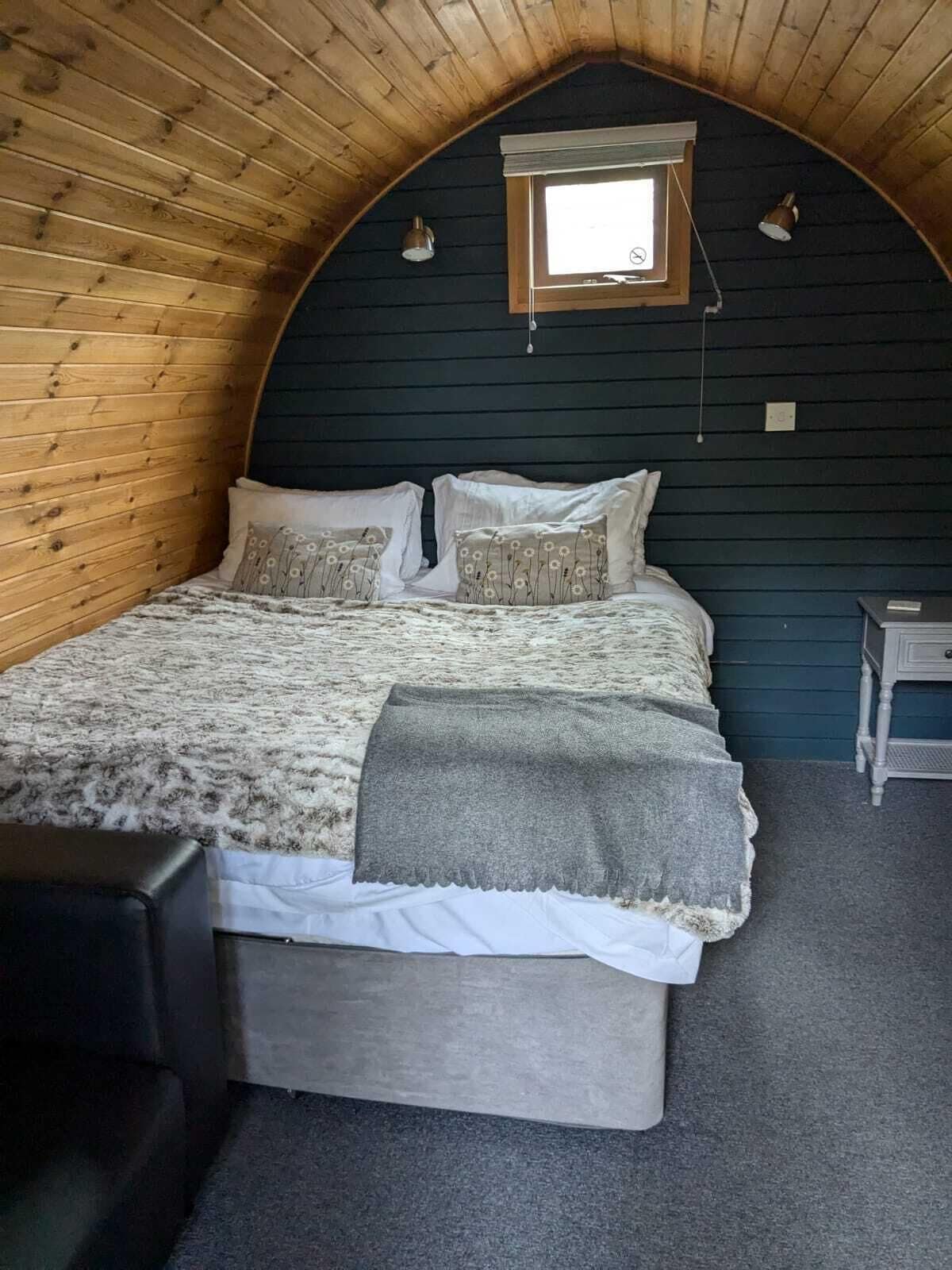 Ein gemütlicher Raum mit Holzwänden, einem Bett, einem kleinen Fenster und einem Nachttisch.