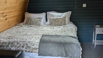 Ein gemütlicher Raum mit Holzwänden, einem Bett, einem kleinen Fenster und einem Nachttisch.