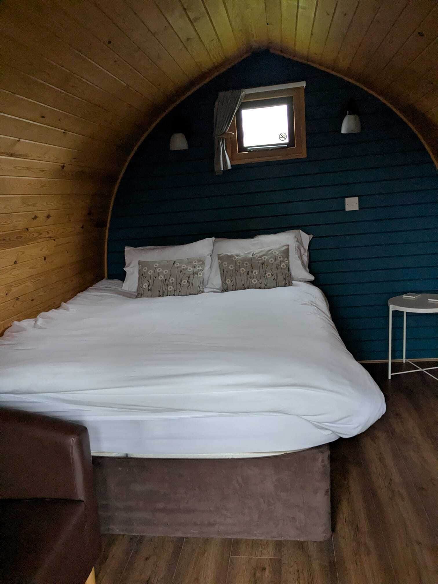 A cozy, single-room cabin with a sloped ceiling, a bed with white bedding, and a small table by the window.